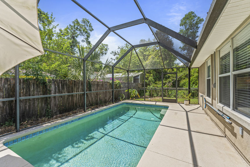 Backyard view of in-ground pool surrounded by privacy fencing and greenery in St. Augustine Florida