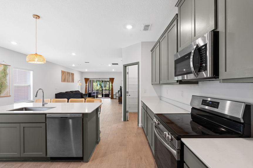 Spacious kitchen with stainless steel appliances, green cabinetry, and view into open living area in a St Augustine home