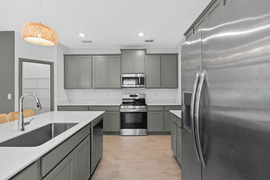 Spacious kitchen with stainless steel appliances, green cabinetry, and view into open living area in a St Augustine home