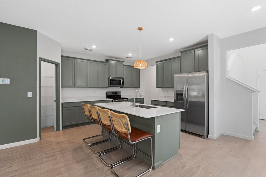 Spacious kitchen with stainless steel appliances, green cabinetry, and view into open living area in a St Augustine home