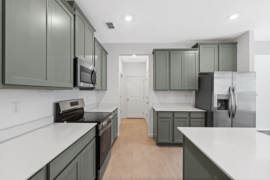 Spacious kitchen with stainless steel appliances, green cabinetry, and view into open living area in a St Augustine home