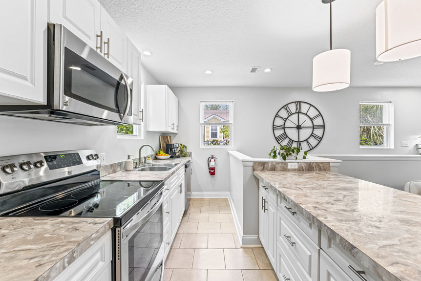 Bright modern kitchen with stainless steel appliances, white cabinetry, and marble countertops in a St. Augustine home