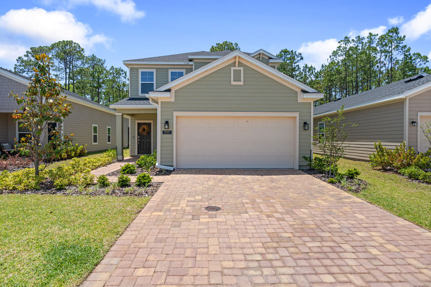 Front view of two-story home with paved driveway, landscaped yard, and two-car garage in St Augustine, Florida
