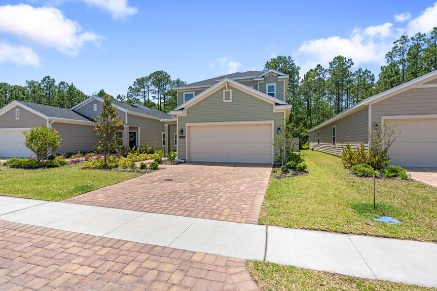 Front view of two-story home with paved driveway, landscaped yard, and two-car garage in St Augustine, Florida