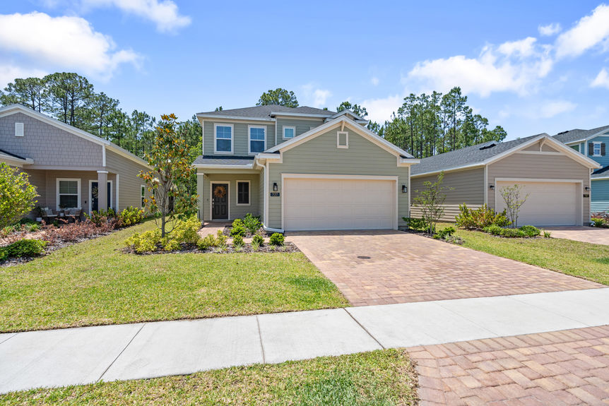 Front view of two-story home with paved driveway, landscaped yard, and two-car garage in St Augustine, Florida