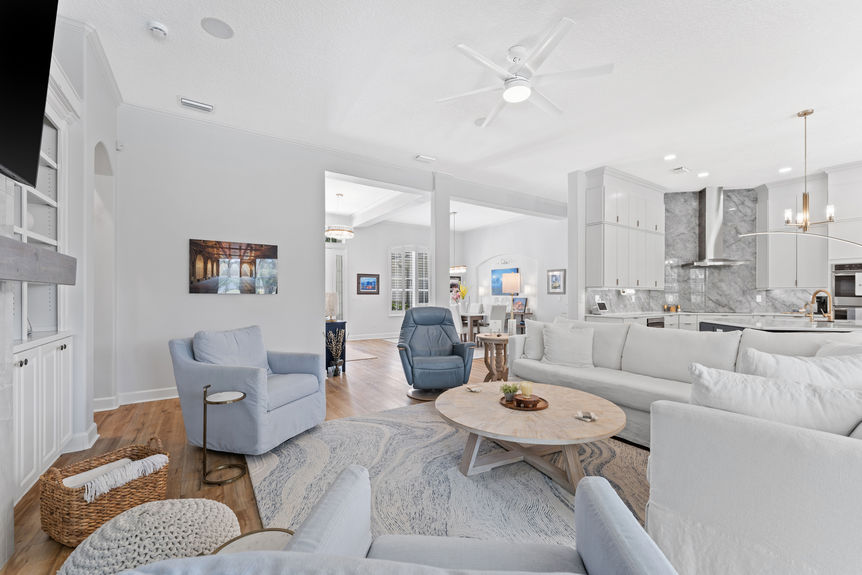 Open-concept living space with white sofas, modern decor, and view into kitchen