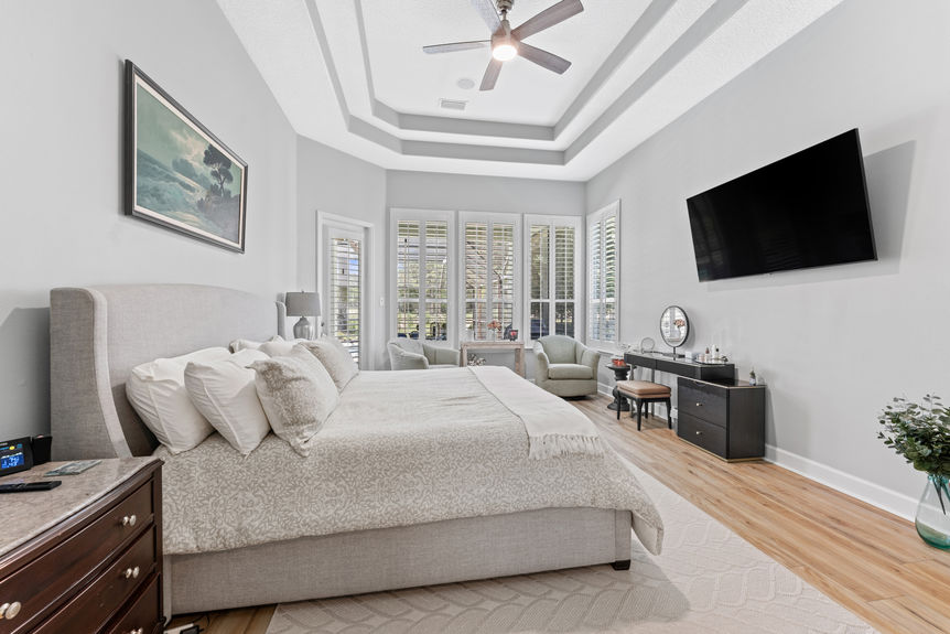 Master bedroom with tray ceiling, large windows, and cozy sitting area in a St Augustine Florida home