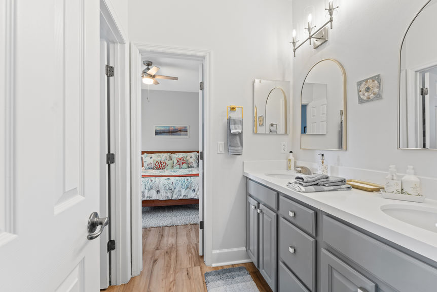 Bathroom with double sinks and view into guest bedroom with beach decor