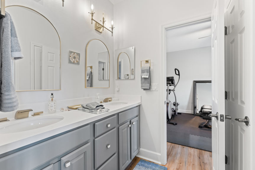 Double vanity bathroom with arched mirrors and doorway to home gym