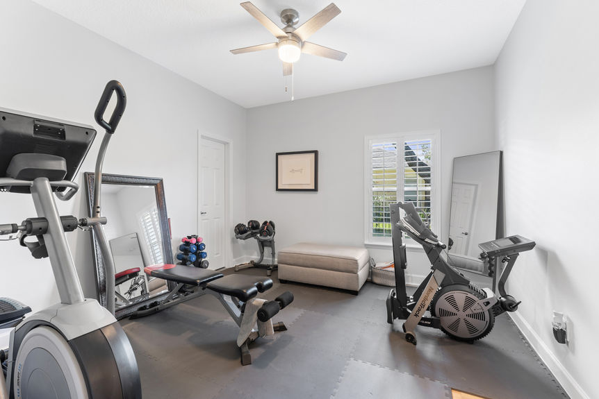 Home gym with cardio machines, free weights, and large mirror in bright room