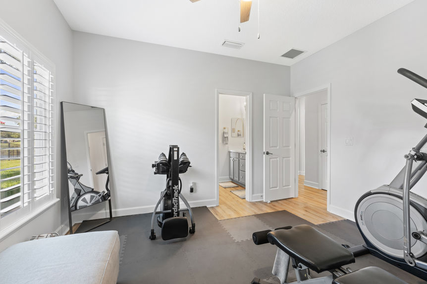 Home gym with cardio machines, free weights, and large mirror in bright room