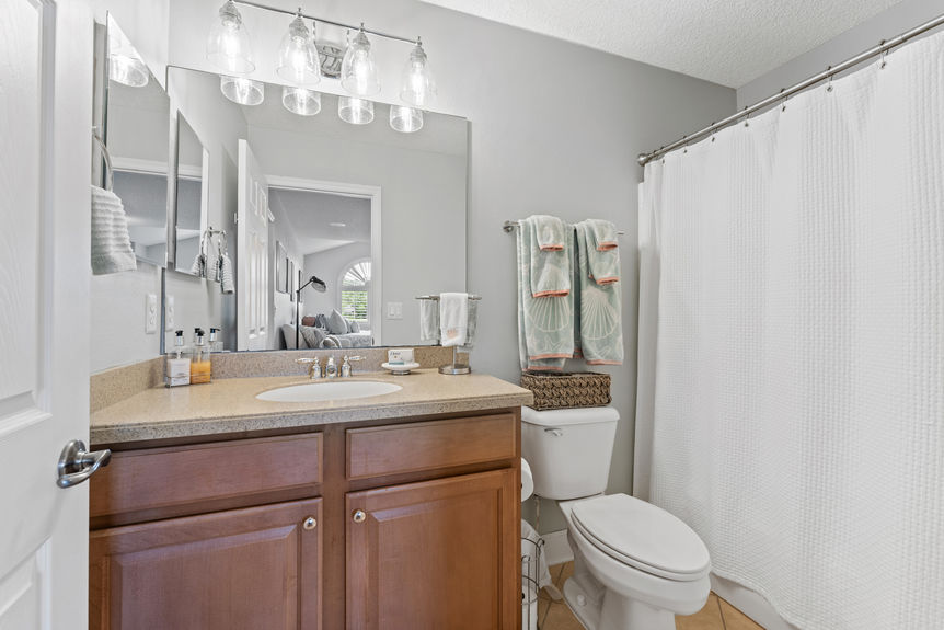 Bathroom with single sink vanity, toilet, and shower curtain next to upstairs living space