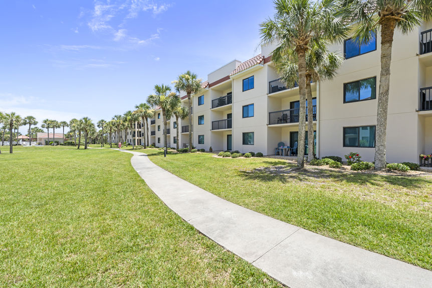 Front view of Ocean Village Club condo building with palm trees and walkways