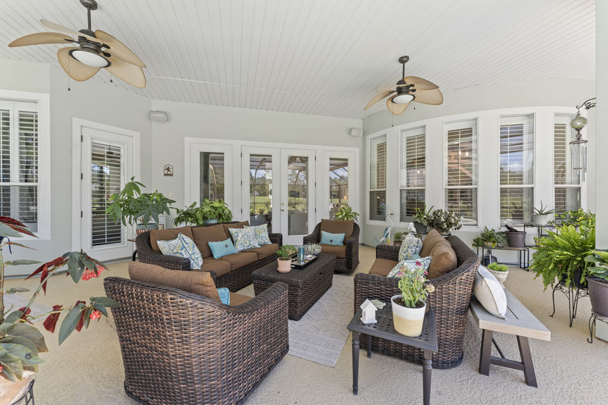 Outdoor patio with wicker furniture, ceiling fans, and lush potted plants in Florida home