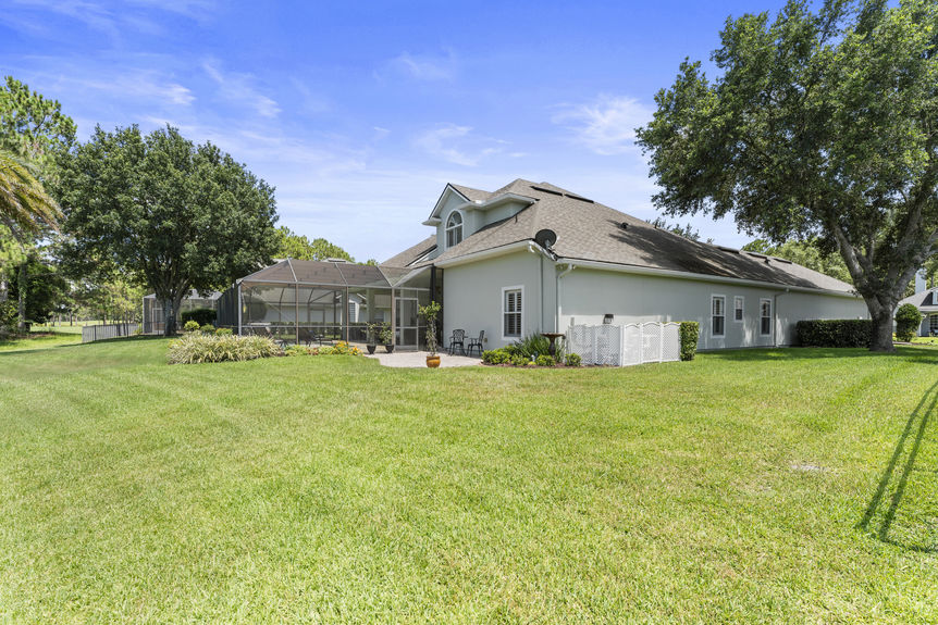 Large backyard with grass lawn, trees, and view of screened-in patio and pool area
