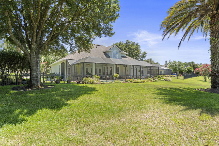 Large backyard with grass lawn, trees, and view of screened-in patio and pool area