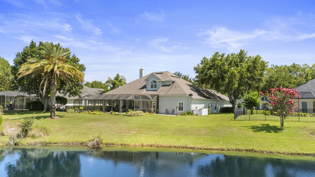 Large backyard with grass lawn, trees, and view of screened-in patio and pool area