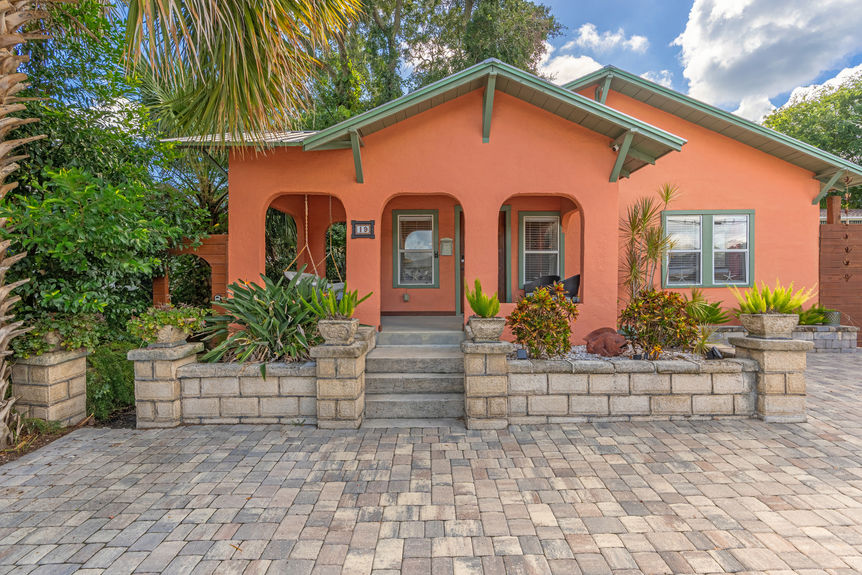 Front view of a vibrant orange Mediterranean-style home with arched porch, paver driveway, and tropical landscaping in St Augustine, Florida.