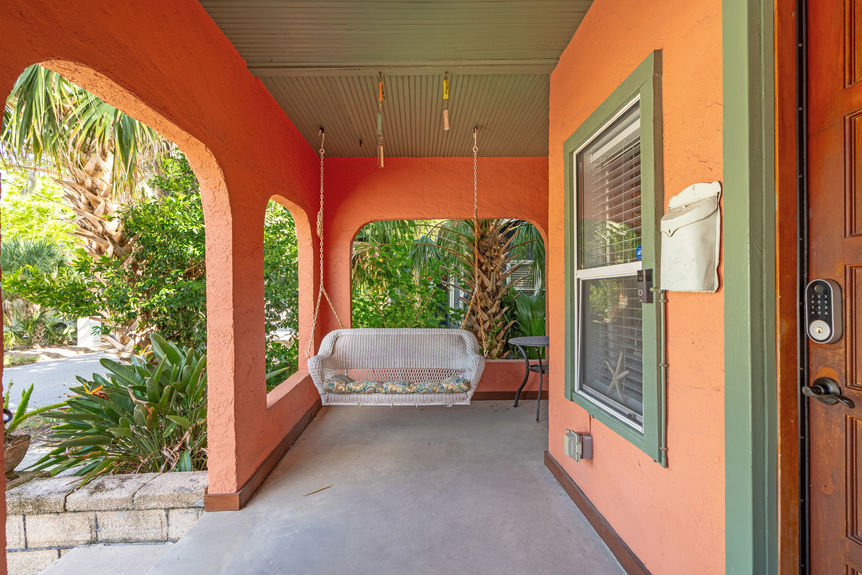 Covered front porch with arched openings, wicker seating, and tropical landscaping at a St Augustine Florida home for sale.