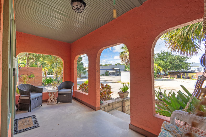 Covered front porch with arched openings, wicker seating, and tropical landscaping at a St Augustine Florida home for sale.