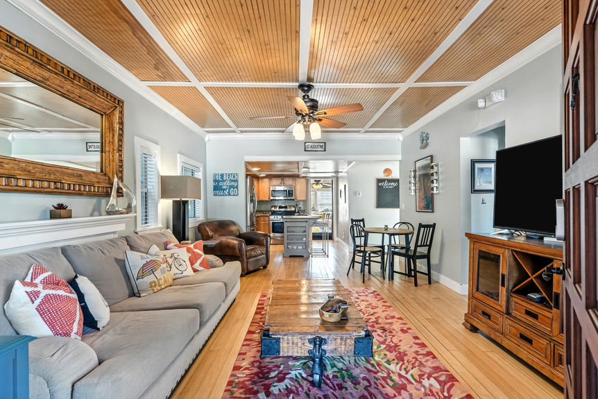 Cozy living room with gray sofa, rustic coffee table, wood ceiling accents, and open kitchen layout in a St Augustine Florida home for sale.