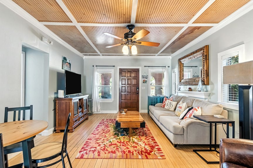 Cozy living room with gray sofa, rustic coffee table, wood ceiling accents, and open kitchen layout in a St Augustine Florida home for sale.