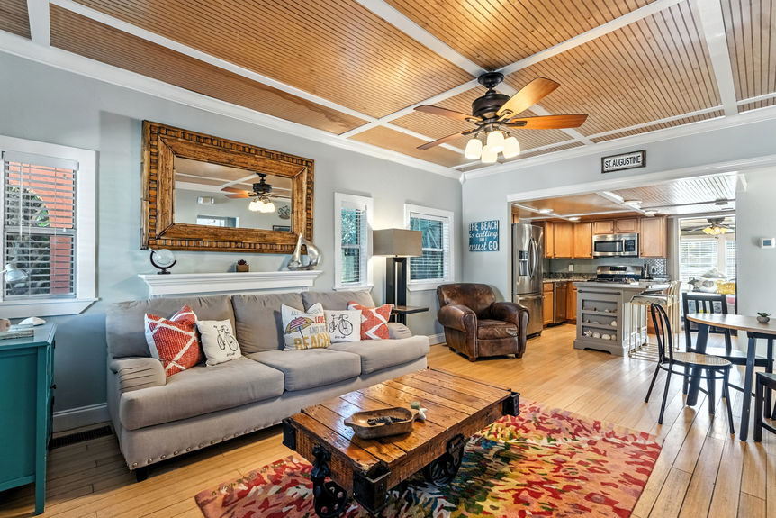 Cozy living room with gray sofa, rustic coffee table, wood ceiling accents, and open kitchen layout in a St Augustine Florida home for sale.
