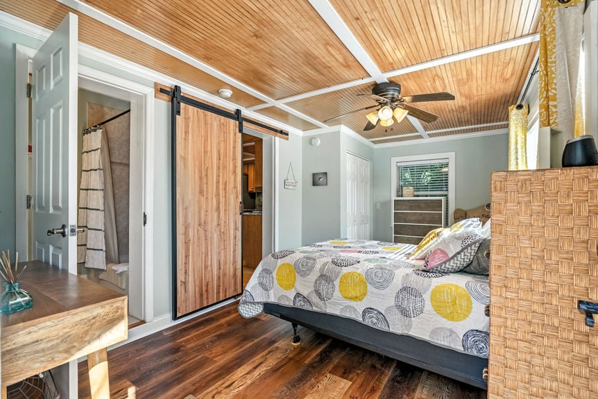 Cozy bedroom with wood ceiling, large windows, yellow curtains, and colorful patterned quilt in a St Augustine Florida home for sale.