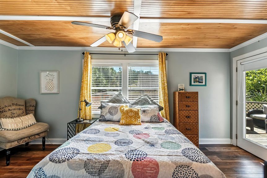 Cozy bedroom with wood ceiling, large windows, yellow curtains, and colorful patterned quilt in a St Augustine Florida home for sale.
