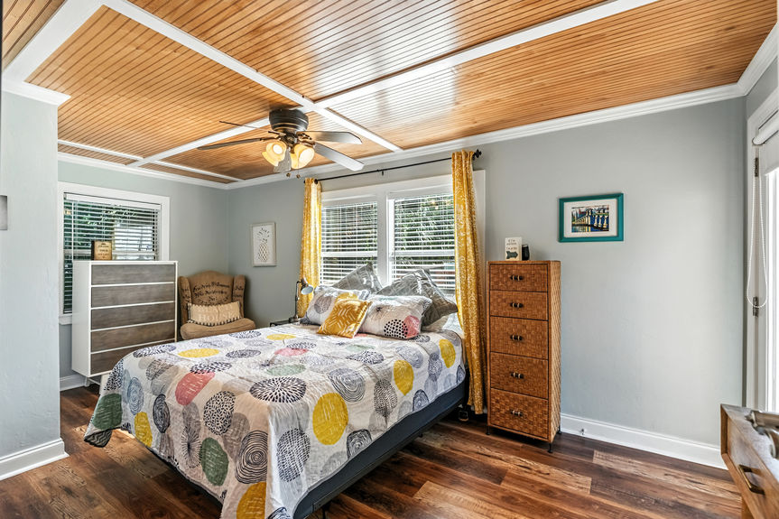 Cozy bedroom with wood ceiling, large windows, yellow curtains, and colorful patterned quilt in a St Augustine Florida home for sale.