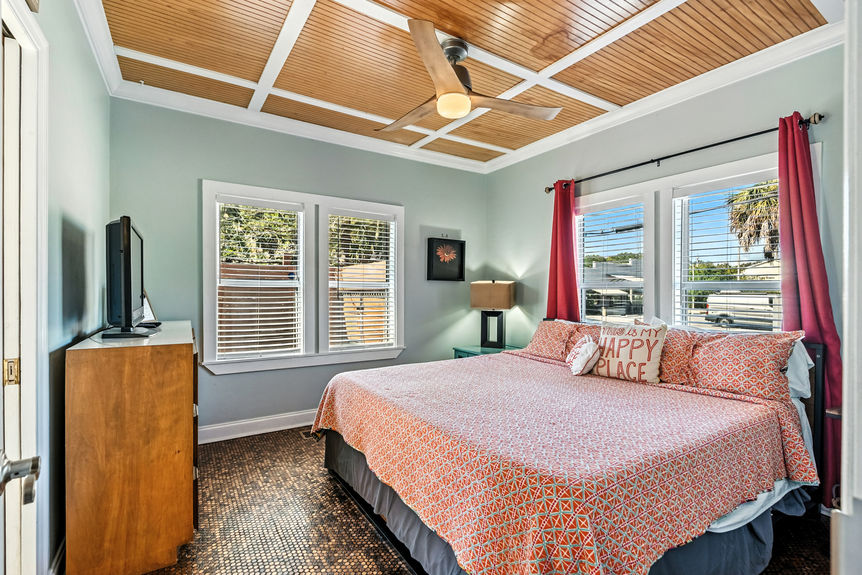 Bright bedroom with wood ceiling, coral bedding, red curtains, and large windows in a St Augustine Florida home for sale.