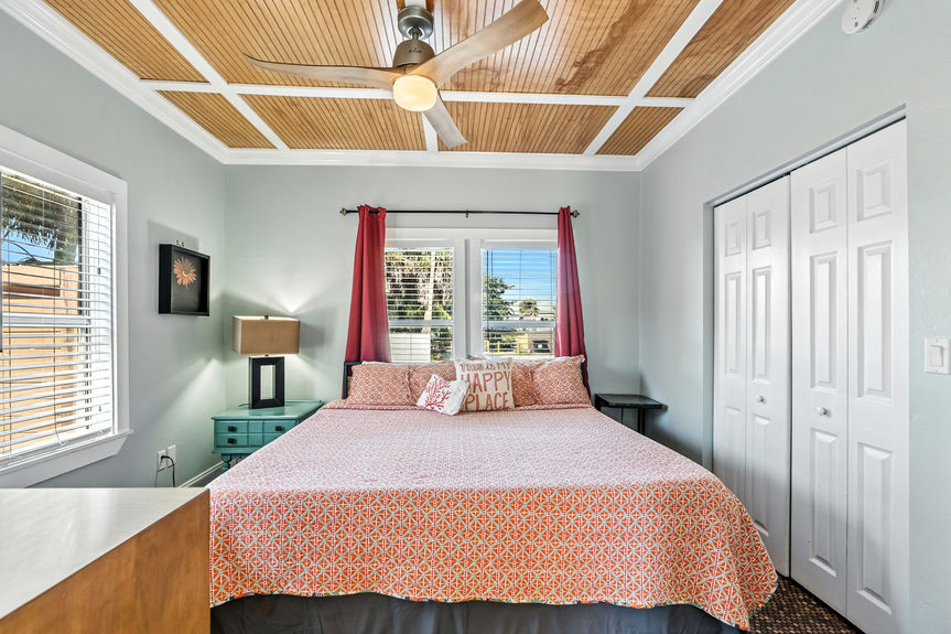 Bright bedroom with wood ceiling, coral bedding, red curtains, and large windows in a St Augustine Florida home for sale.