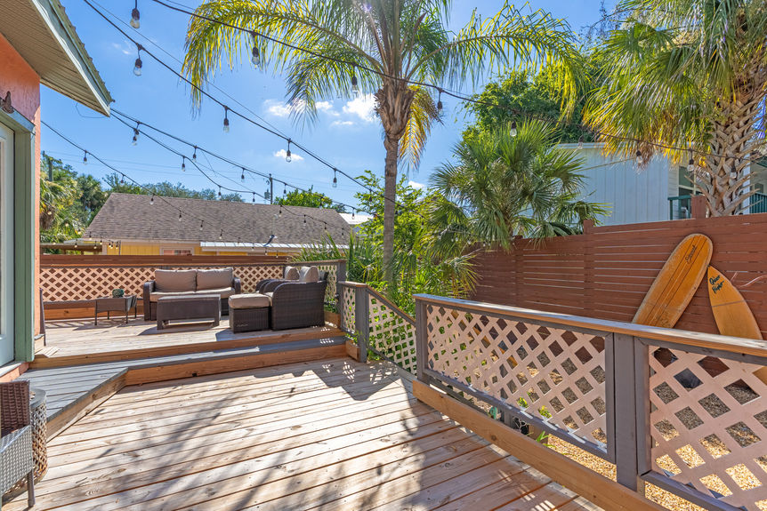 Large wooden backyard deck with wicker furniture, string lights, and palm trees at a St Augustine Florida home for sale.