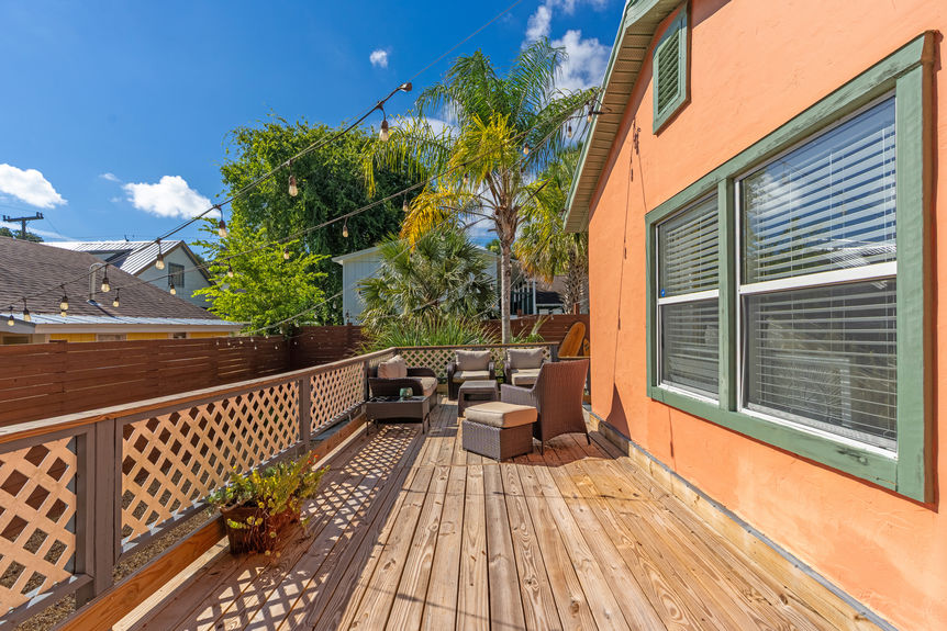 Large wooden backyard deck with wicker furniture, string lights, and palm trees at a St Augustine Florida home for sale.