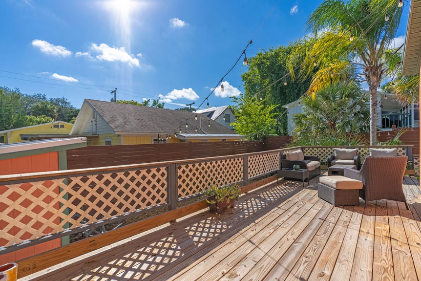 Large wooden backyard deck with wicker furniture, string lights, and palm trees at a St Augustine Florida home for sale.
