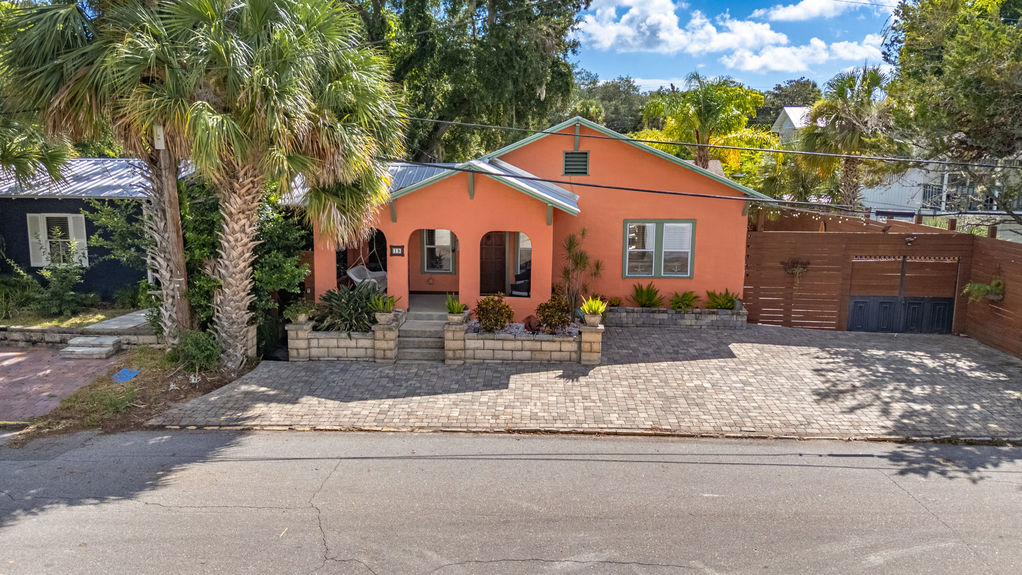 Front view of a vibrant orange Mediterranean-style home with arched porch, paver driveway, and tropical landscaping in St Augustine, Florida.