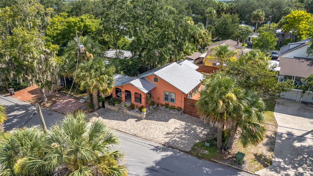 Angled aerial shot of St Augustine Florida home with orange exterior, metal roof, private backyard, and large wooden deck with outdoor seating.