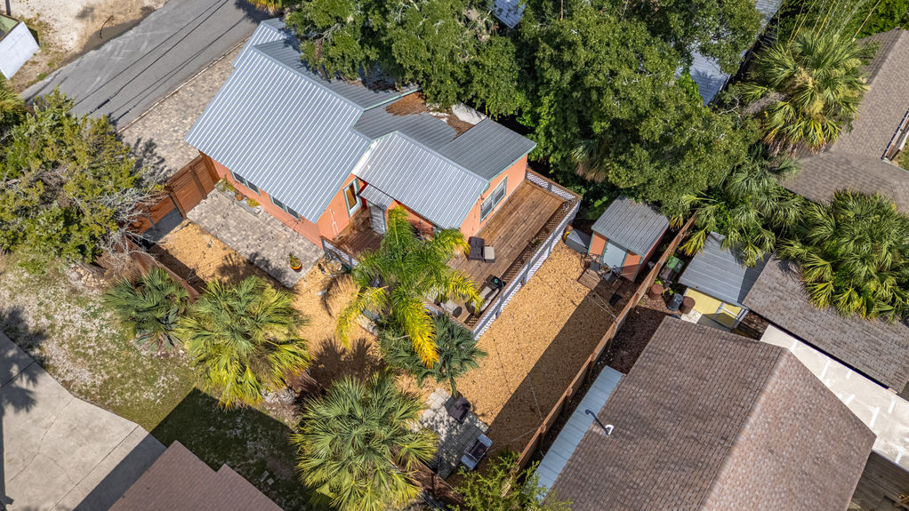 Angled aerial shot of St Augustine Florida home with orange exterior, metal roof, private backyard, and large wooden deck with outdoor seating.