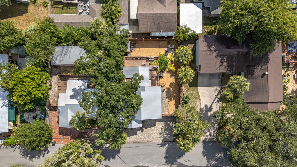 Overhead drone view of a St Augustine Florida home with metal roof, backyard deck, and tropical landscaping surrounded by neighboring houses.