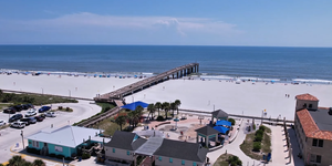 Aerial view of St. Augustine Beach Pier with white sand, blue ocean, and visitors enjoying the shoreline.