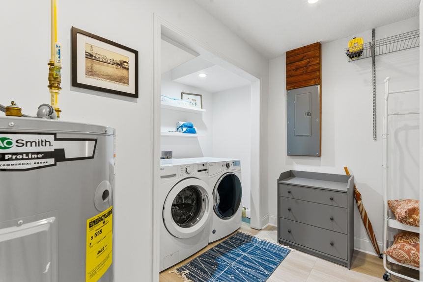 A clean, white utility room containing a high-efficiency washer and dryer set, an AO Smith water heater, a grey dresser for storage, and open shelving.