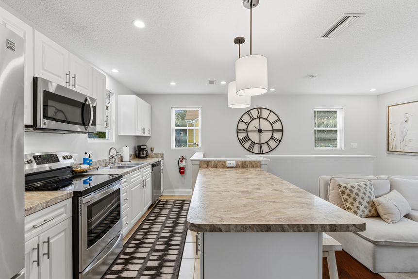 Contemporary kitchen featuring white Shaker-style cabinets, stainless steel appliances, marble-patterned laminate countertops, and pendant lighting over a breakfast bar with white stools.