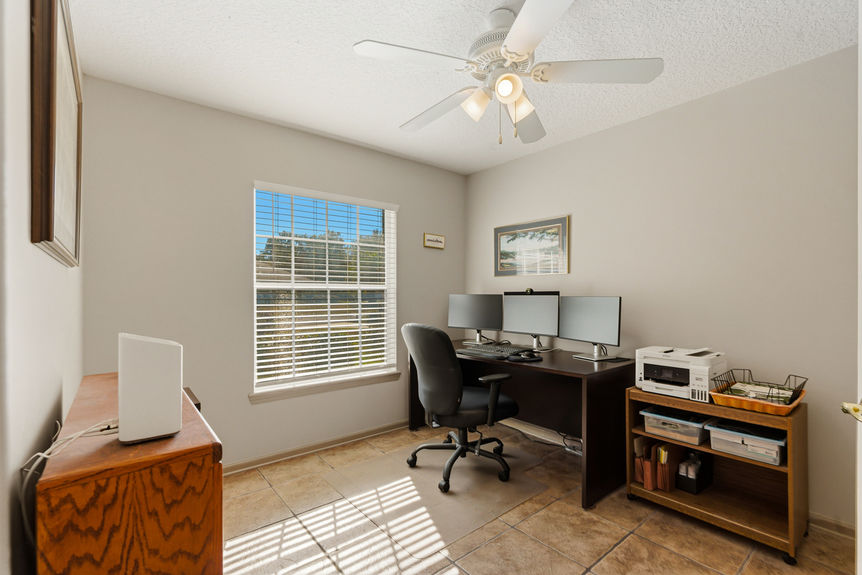 Homes for Sale in St. Johns, Florida: A bright home office or bedroom featuring hardwood-style flooring, a wooden desk with a computer setup, and a window overlooking a fenced backyard.