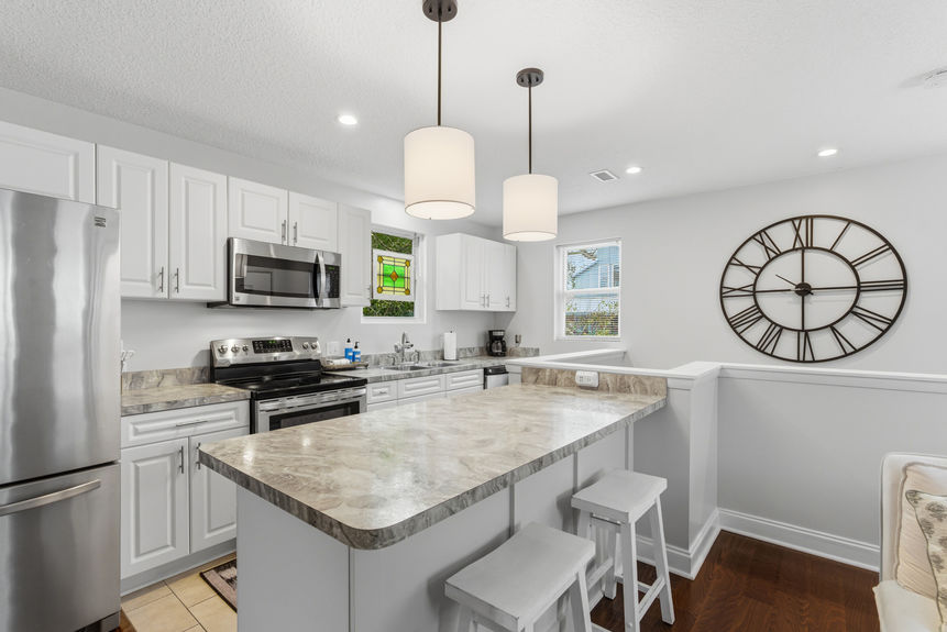 Contemporary kitchen featuring white Shaker-style cabinets, stainless steel appliances, marble-patterned laminate countertops, and pendant lighting over a breakfast bar with white stools.