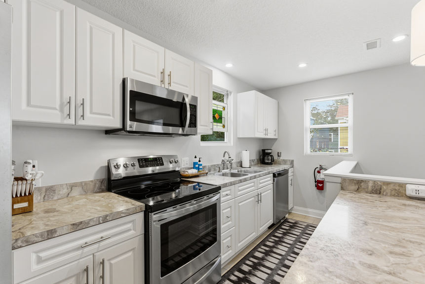 Contemporary kitchen featuring white Shaker-style cabinets, stainless steel appliances, marble-patterned laminate countertops, and pendant lighting over a breakfast bar with white stools.