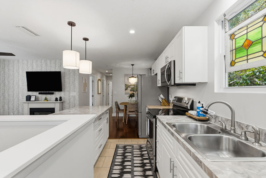 A bright kitchen featuring white Shaker-style cabinets, stainless steel appliances, a double-basin sink, and a unique decorative stained glass window insert.
