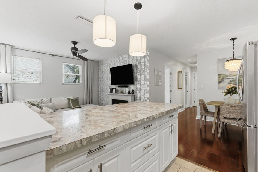 Contemporary kitchen featuring white Shaker-style cabinets, stainless steel appliances, marble-patterned laminate countertops, and pendant lighting over a breakfast bar with white stools.