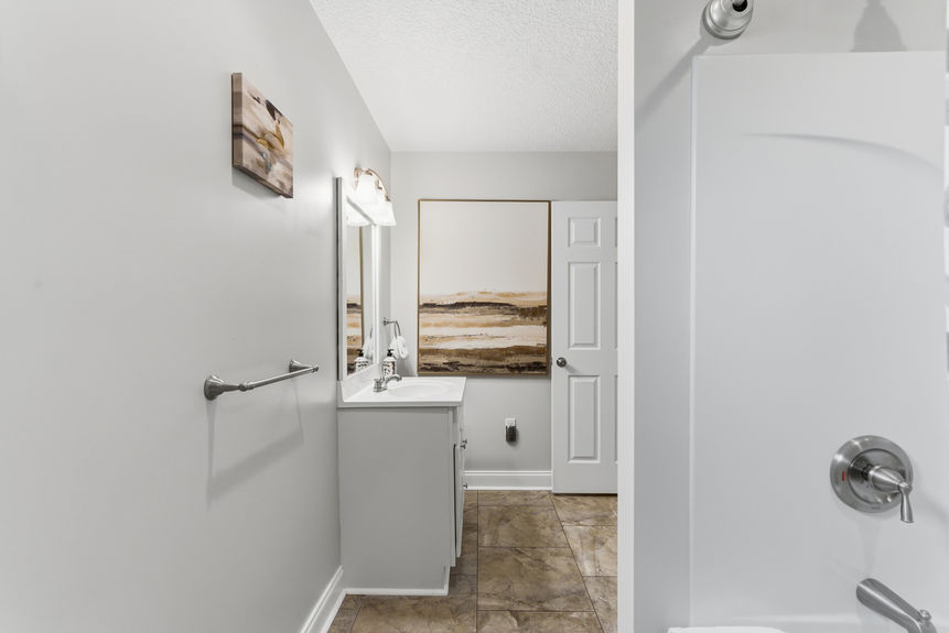 Modern bathroom with a double sink white vanity, large mirror with bell-shaped lights, and a white sliding pocket door leading into a carpeted walk-in closet.