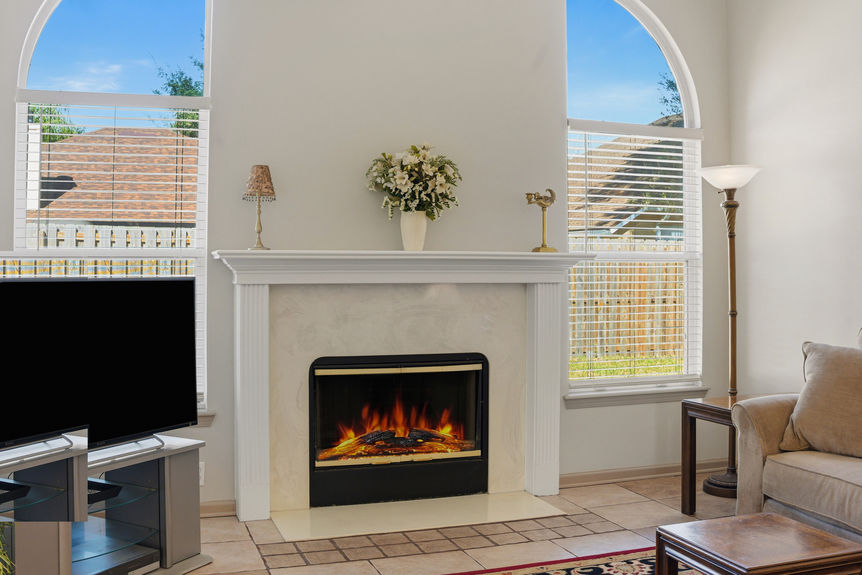Homes for Sale in St. Johns, Florida: A bright living room featuring a white mantle fireplace, large arched windows with blinds, and neutral tile flooring.