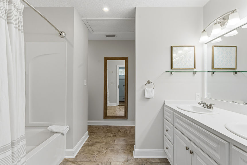 Modern bathroom with a double sink white vanity, large mirror with bell-shaped lights, and a white sliding pocket door leading into a carpeted walk-in closet.